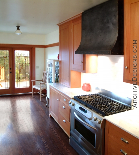 A distressed steel hood with dome head copper rivets helps anchor a pleasant California bungalow kitchen, by Archive Designs.