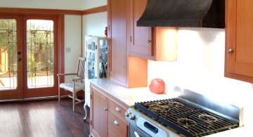 A distressed steel hood with dome head copper rivets helps anchor a pleasant California bungalow kitchen, by Archive Designs.