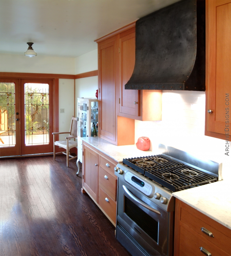 A distressed steel hood with dome head copper rivets helps anchor a pleasant California bungalow kitchen, by Archive Designs.